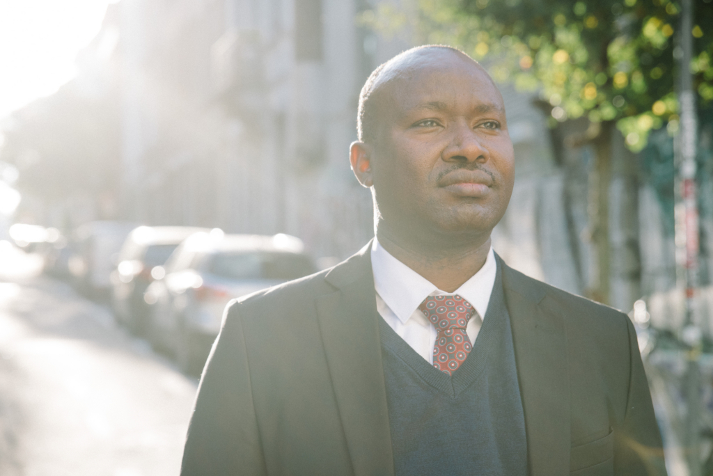 A man stands bathed in sunlight, looking down the street.