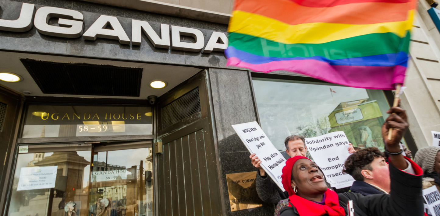 Manifestantes agitan banderas arcoíris delante de un edificio en cuyo portal puede leerse “Casa Uganda”.
