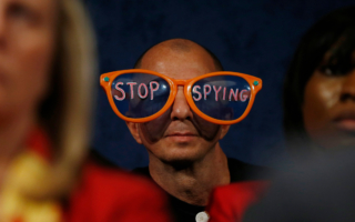 an image of someone at a protest wearing large clown glasses that say 'Stop Spying'