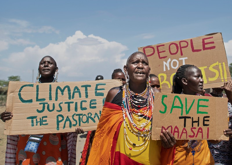 Un grupo de mujeres con la indumentaria tradicional masái sostienen carteles que dicen “Salva a los masáis” y “Personas, no beneficios”.