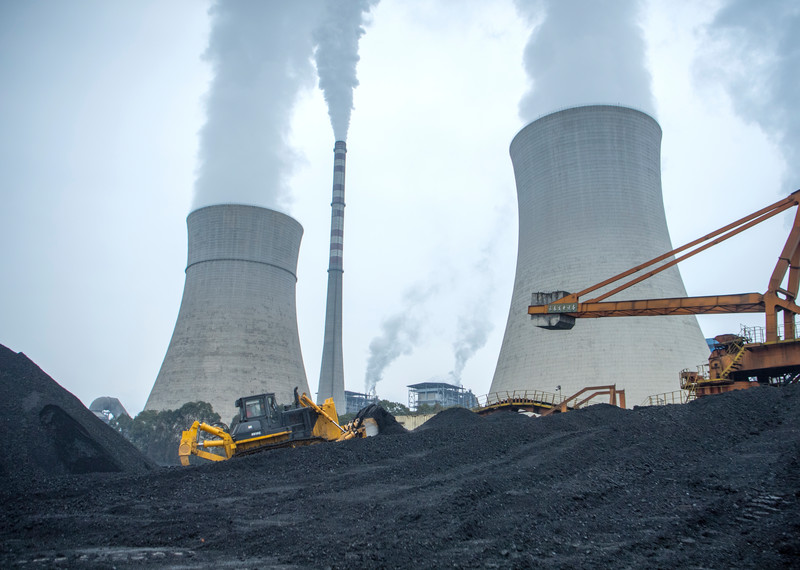 Dos torres enormes de la central eléctrica de Jiangyou (China). Delante de ellas, excavadoras y grúas avanzan con dificultad entre las negras lomas de carbón.