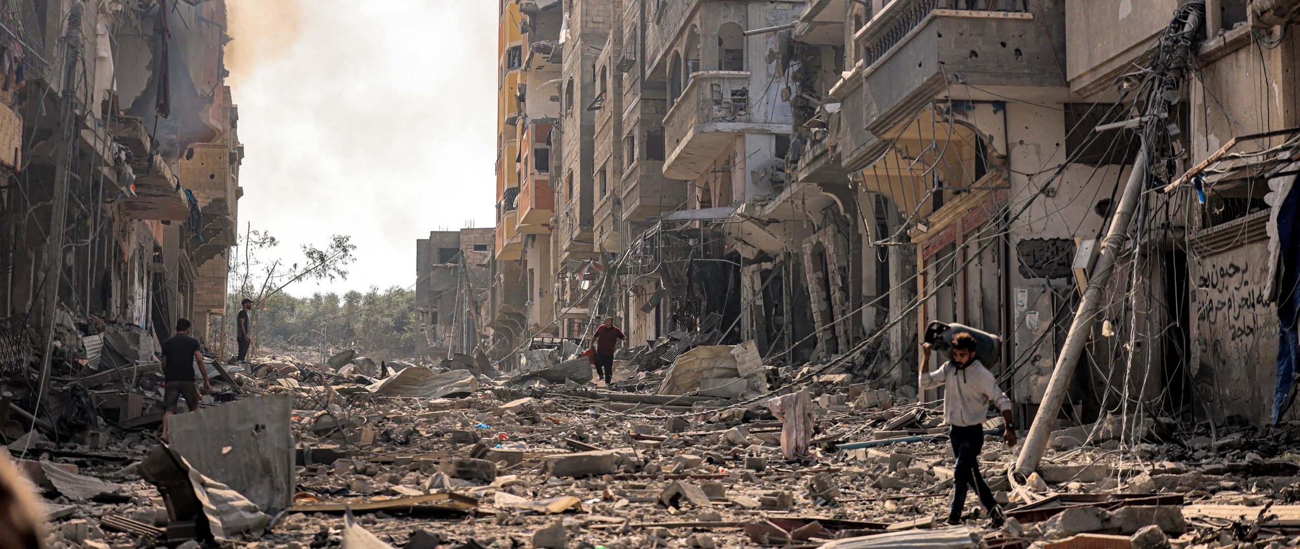 Situación de una área bombardeada en Gaza:  escombros y edificios destruidos por todas partes, mientras un hombre camina sobre los escombros.