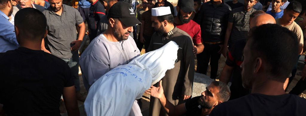 Un hombre lleva en brazos el cadáver de un miembro de la familia Hijazi muerto en un ataque israelí, para que sea enterrado en una sección recién construida de un cementerio de Rafah, en el sur de la Franja de Gaza, el 10 de noviembre de 2023, en medio de los constantes enfrentamientos entre Israel y el grupo palestino Hamás.