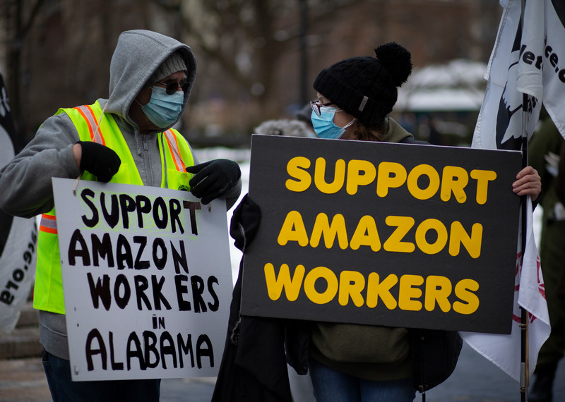 Manifestantes con máscaras sostienen pancartas con el texto “Apoya a los trabajadores y trabajadoras de Amazon”.