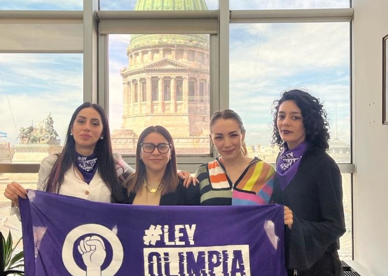 Four women hold up a banner with the words, #Ley Olimpia.A