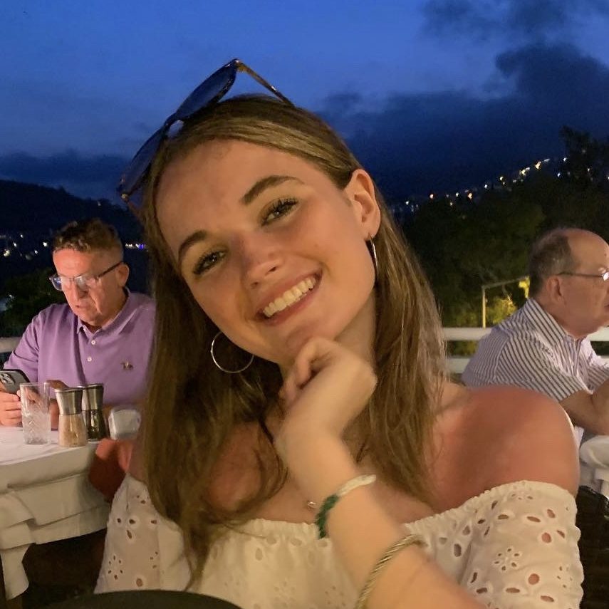 Claudia está sentada en la terraza de un restaurante y posa sonriente con la mano en la barbilla.