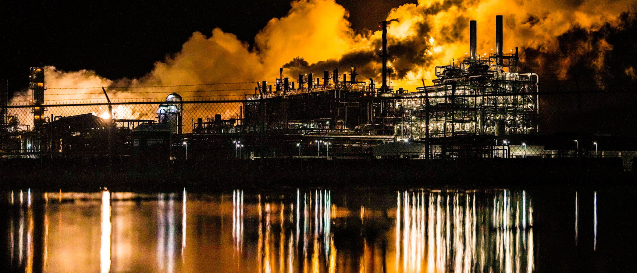 Humo negro y fuego causados por la combustión, o la quema controlada de sustancias, y con frecuencia asociados a emisiones tóxicas y baja calidad del aire, saliendo de una planta cerca del Canal de Navegación de Houston de noche en 2023.
