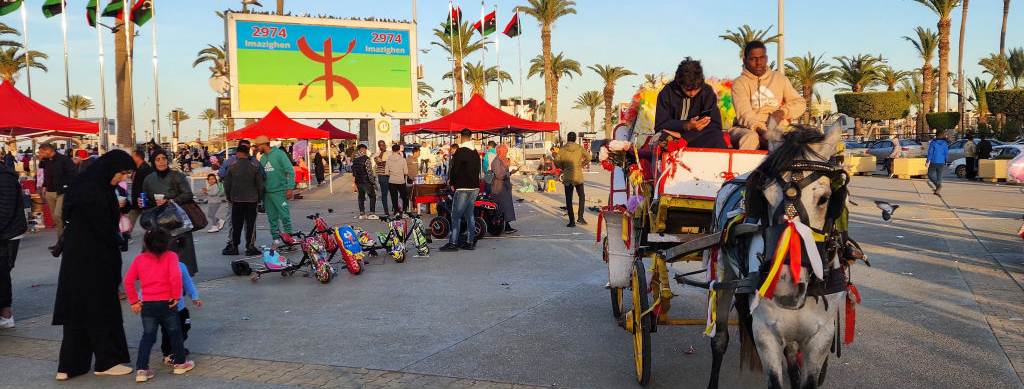 Varias personas montan en un carro tirado por un caballo delante de una valla publicitaria que conmemora el año nuevo amazigh en la plaza de los Mártires de Trípoli, capital de Libia, el 14 de enero de 2024.