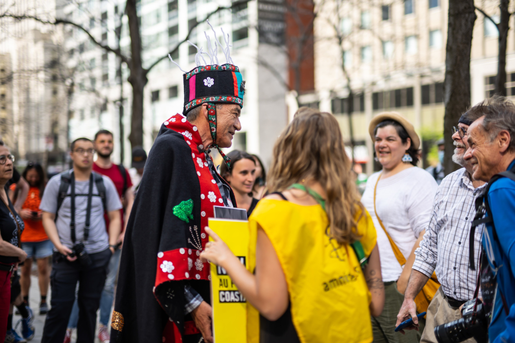 Un líder indígena habla sonríente con otras personas que participan con él en una protesta, muchas de las cuales visten camisetas amarillas de Amnistía.