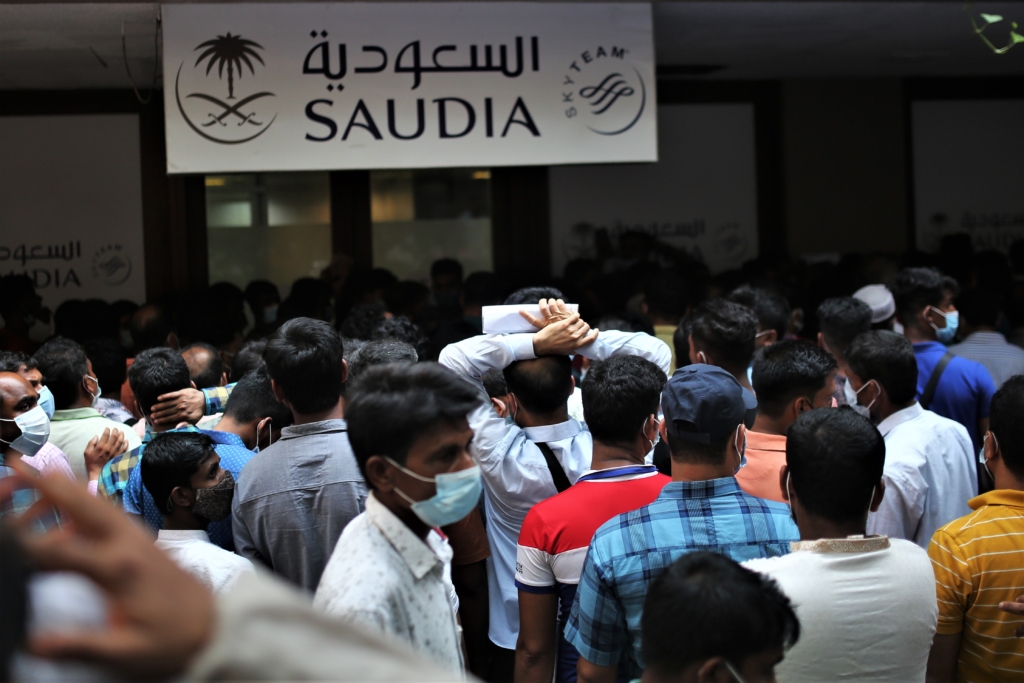 Grupo grande de trabajadores migrantes, muchos de Bangladesh, esperan juntos en un aeropuerto de Arabia Saudí.