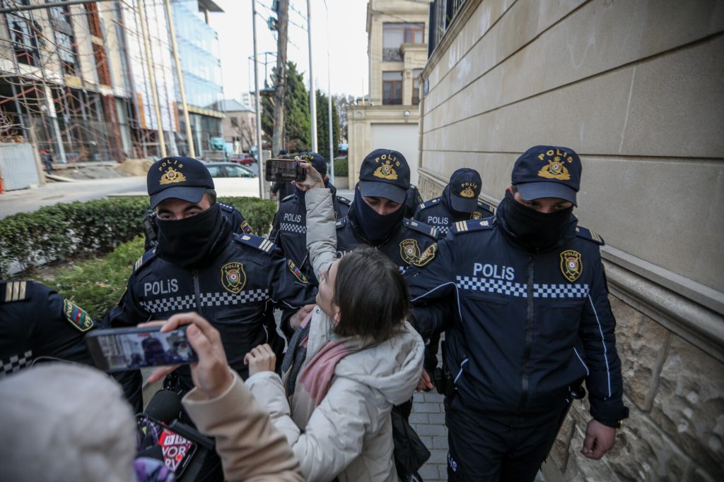 a group of police officers escort someone out of a building. The person being arrested is recording the arrest on a smart phone