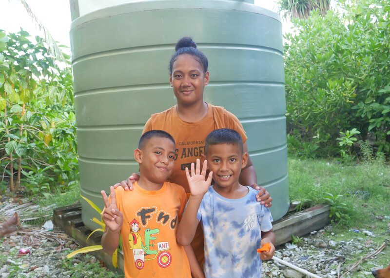 Una familia de Tuvalu, la madre y sus dos hijos, en el exterior de una casa.
