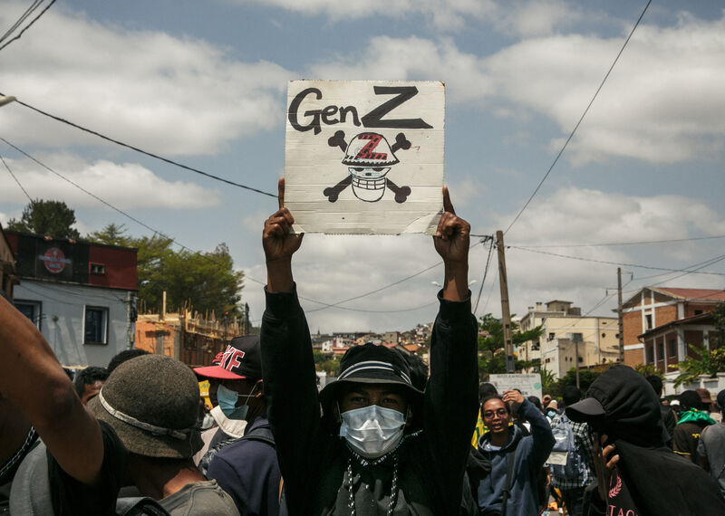 Entre la multitud, un manifestante con sombrero y el rostro cubierto sostiene una pancarta con la inscripción “Gen Z” y una calavera con tibias cruzadas.