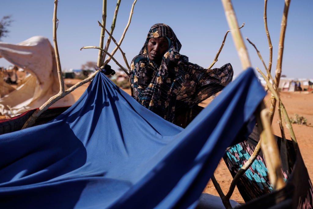 Una mujer monta un alojamiento provisional con grandes trozos de tela atados a ramas.