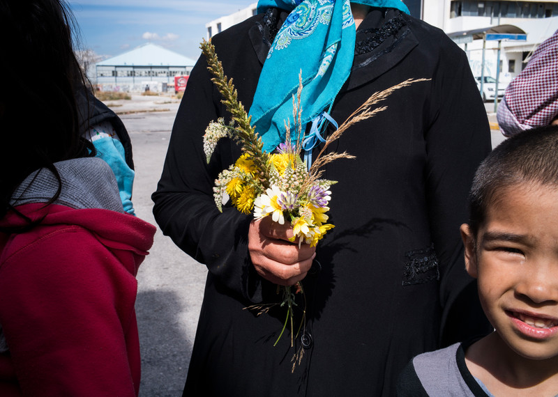 Fuera de la antigua terminal del aeropuerto de Atenas, los niños corretean mientras pasan coches a toda velocidad. Fawzia, una mujer que lleva la cabeza cubierta con un pañuelo azul, recoge flores; un atisbo de belleza entre la basura y el hormigón en proceso de deterioro. © Amnesty International/Olga Stefatou