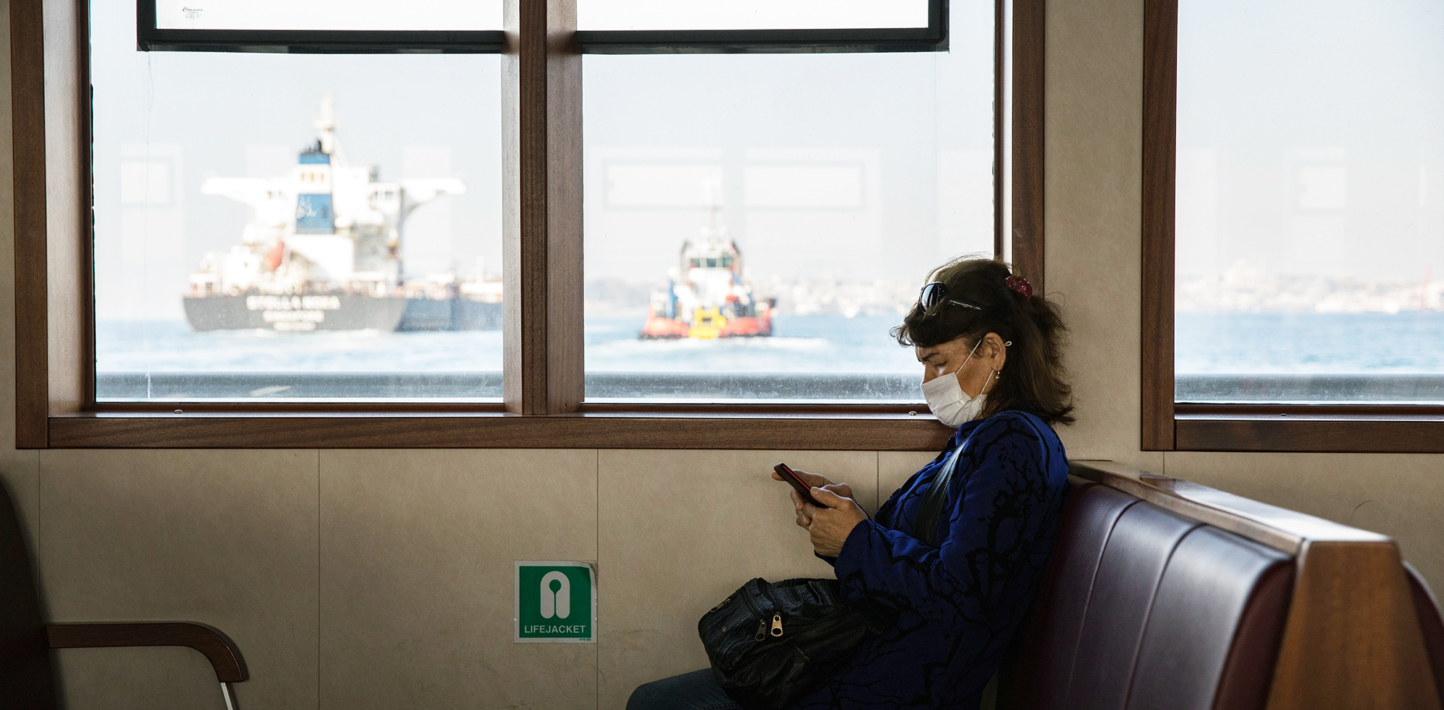 Una mujer con mascarilla contra la COVID-19 en un transbordador público vacío mira su teléfono, Estambul (Turquía), 27 de abril de 2020.