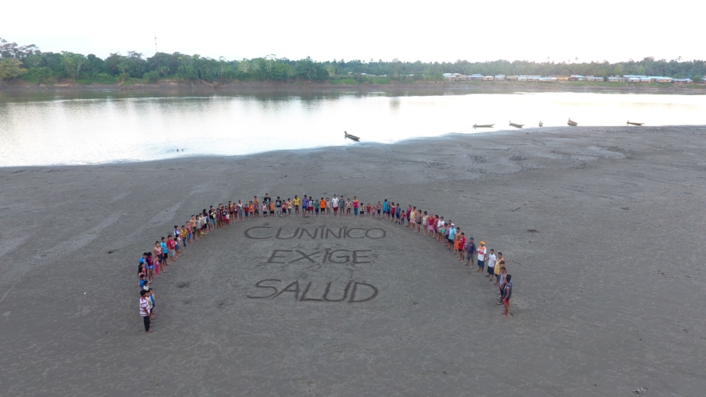 Residentes de Cuninico de pie junto a un mensaje escrito en la arena que dice 