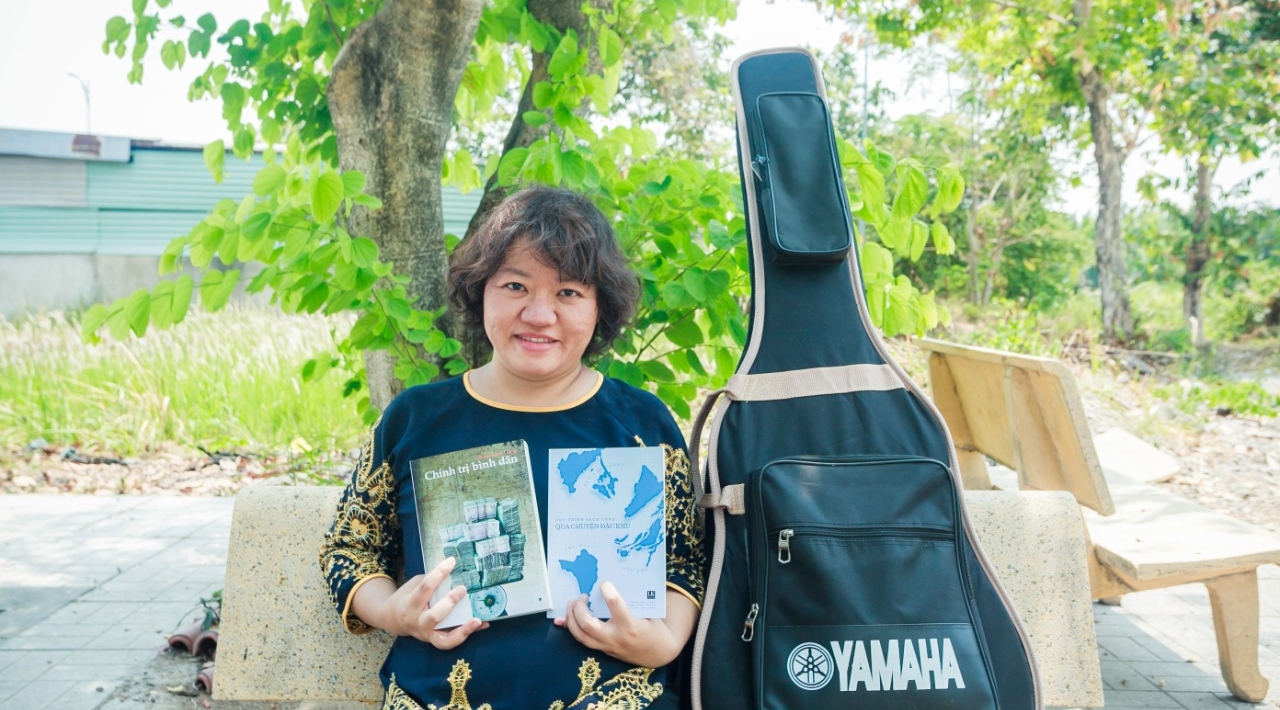 Retrato de Pham Doan Trang, posando con libros y su guitarra.