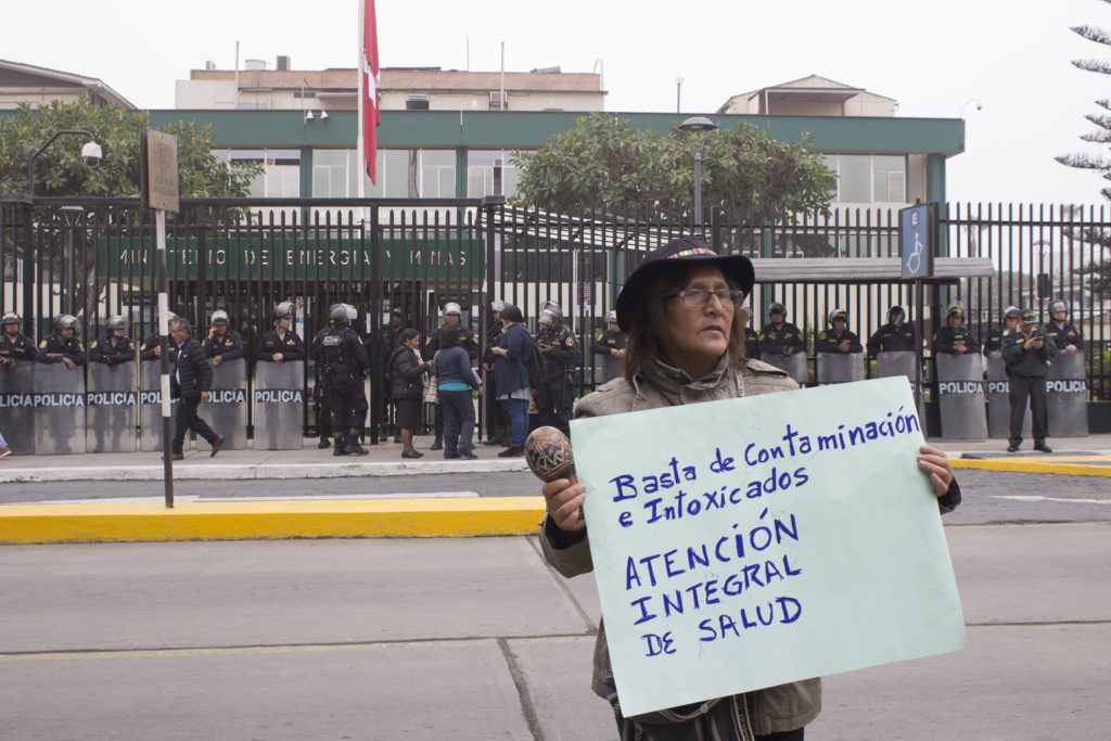 Una miembra de la Plataforma Nacional protestando fuera del Ministerio de Energía y Minas, con un cartel  que dice No más contaminación e intoxicación - Atención integral de la salud. Foto: Jackeline Cárdenas / Convoca.pe, 2019