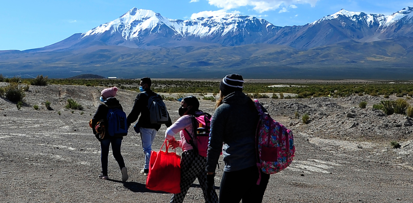 Venezuelan migrants walk before snowcapped mountains in the outskirts of Pisiga, Bolivia, on their way to Colchane, Chile