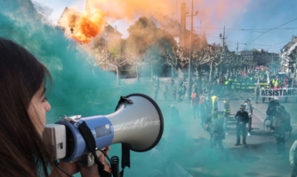 Una manifestante habla por un megáfono en medio de nubes de humo coloreadas provocadas por bombas de humo cerca de personas que participan en la concentración anual del Día Internacional del Trabajo en Estrasburgo (este de Francia), el 1 de mayo de 2019.