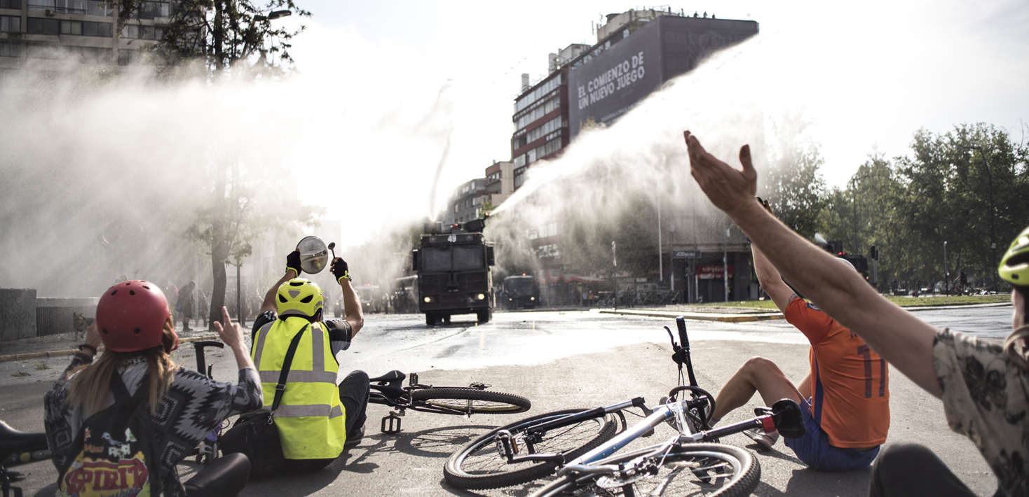 Personas sentadas en las calles con las manos en alto y sus bicicletas tiradas en el suelo mientras un tanque de cañón de agua los golpeaba durante el malestar social en Chile.