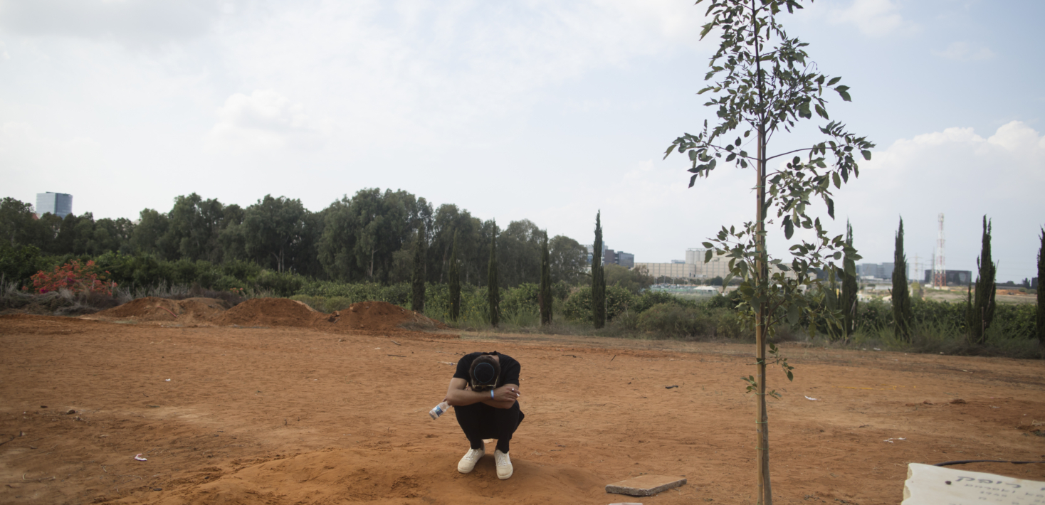 Un homme seul est accroupi en position foetale au milieu d'un terrain de terre battue