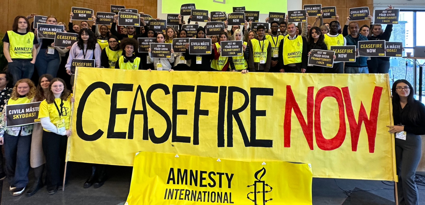 Un groupe de militants et militantes d'Amnesty Suède se tiennent devant une grande bannière qui indique "ceasefire now" pour demander un cessez-le-feu
