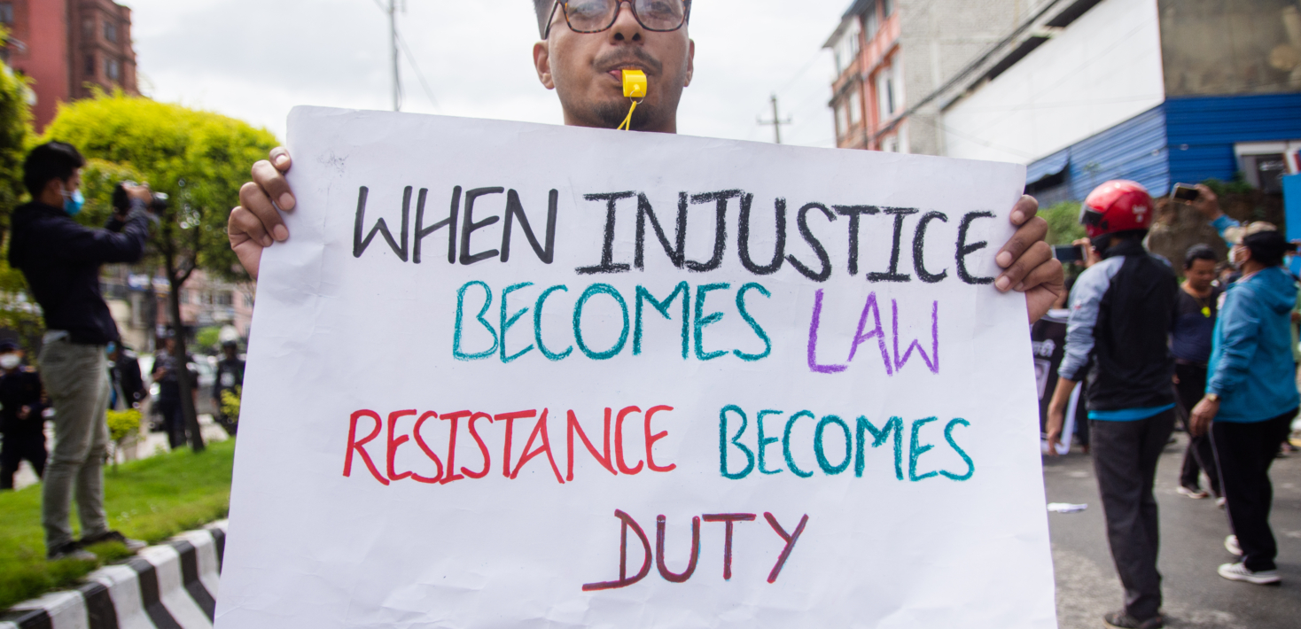 Un manifestant tient une affiche qui indique en anglais "quand l'injustice devient la loi, la résistance devient un devoir"