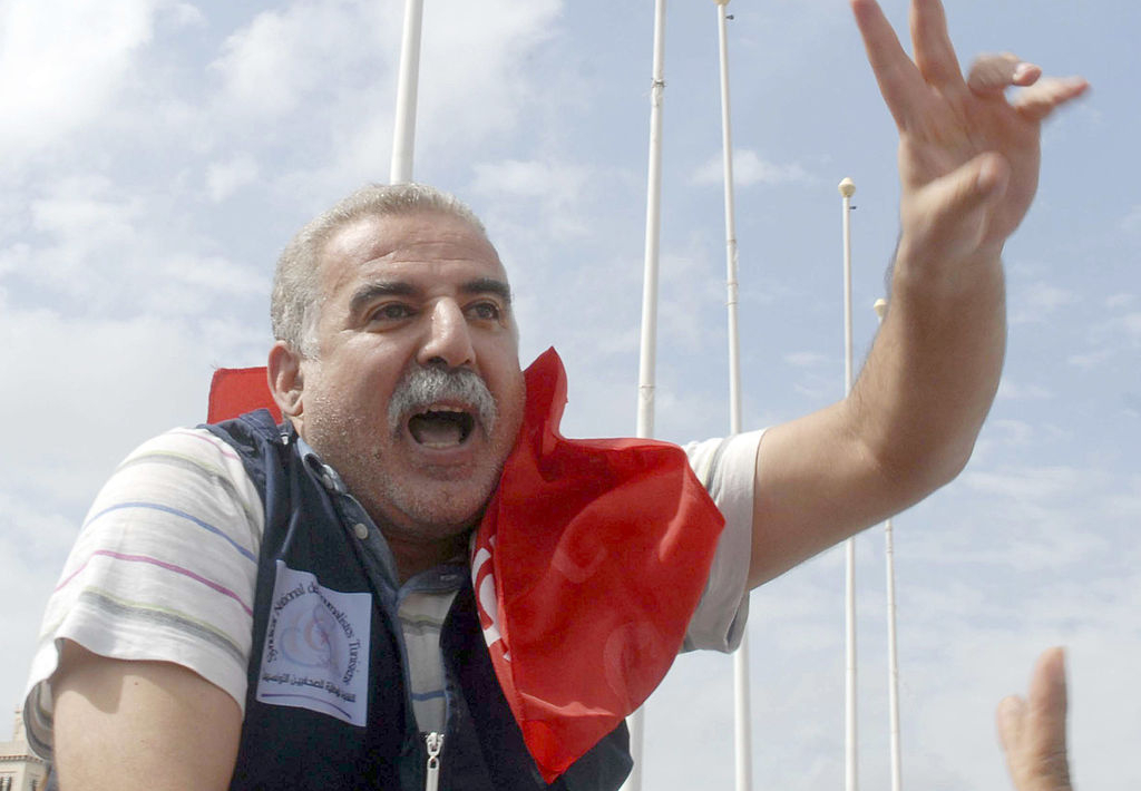 Photo du journaliste Zied el Heni souriant, faisant le signe de la victoire et avec un drapeau tunisien autour du cou