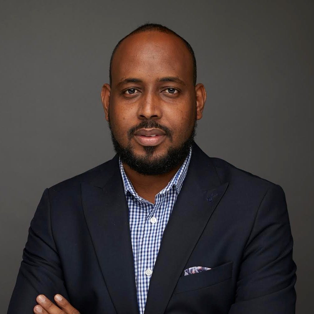 Headshot of Abdullahi, arms folded, wearing a suit, smiling confidently.
