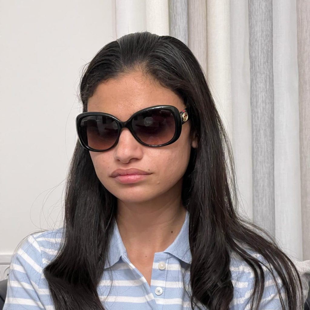 Budour wearing large sunglasses and a blue polo shirt.