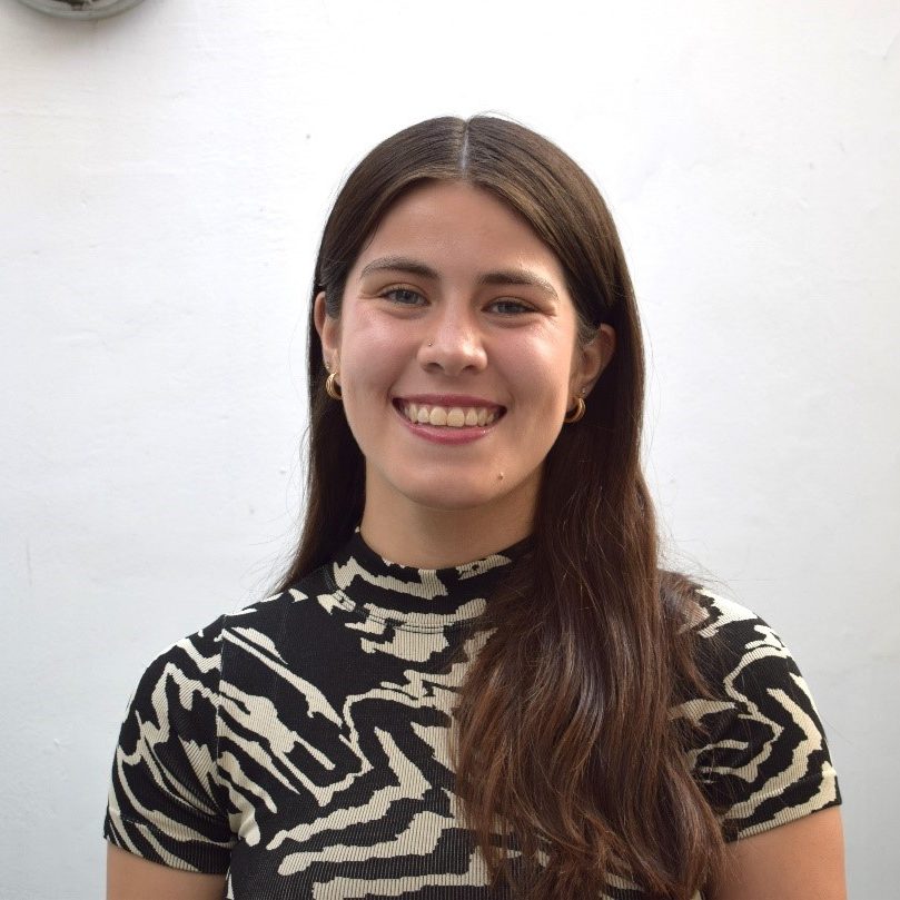 Bernadita is smiling and standing in front of a white wall, wearing a black and white swirled pattern top.