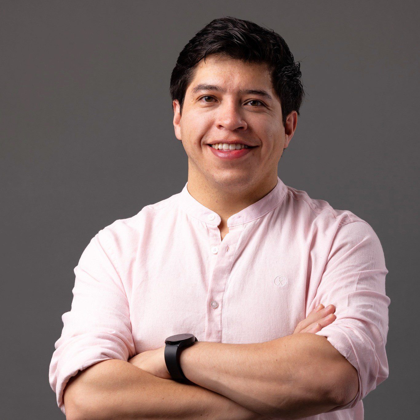Eduardo is smiling, folding his arms across his chest and wearing a pale pink shirt.