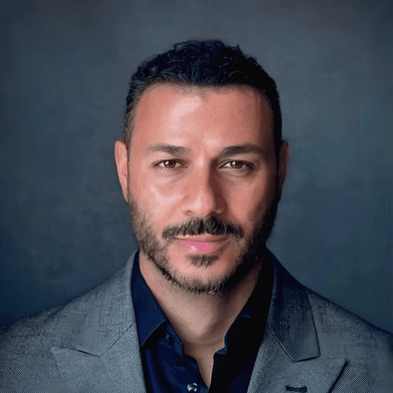 Portrait de Karl Shuker, vêtu d’une veste de costume grise et d’une chemise bleu marine.