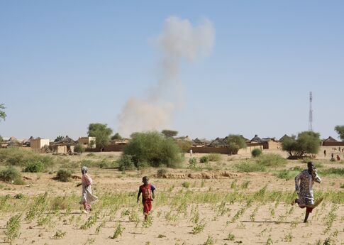 people flee outside a village as smoke rises in the background