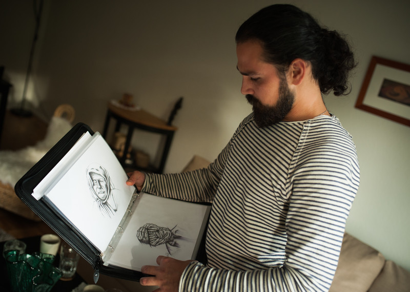 Hennan observe ses nouveaux dessins. Il a dû abandonner toutes ses précédentes réalisations avant de fuir Alep. © Amnesty International
