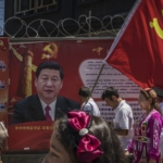 Ethnic Uyghur members of the Communist Party of China carry a flag past a billboard of Chinese President Xi Jinping